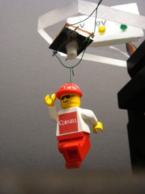 Lego man model hanging from adhesive device
