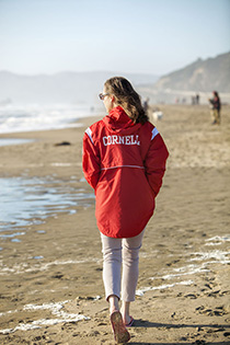Person in Cornell jacket strolls on a West Coast beach